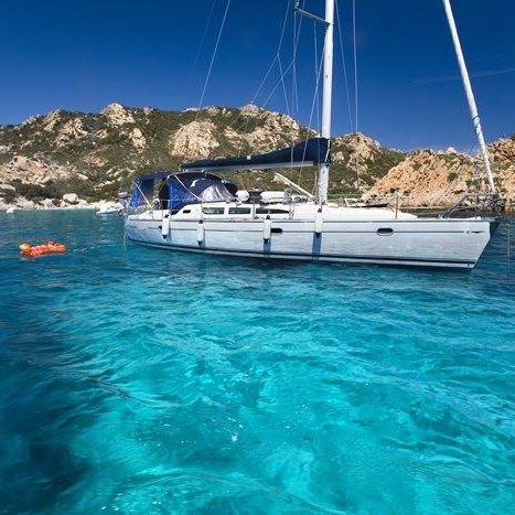 Segelyacht im klaren, türkisfarbigem Wasser mit Bergen im Hintergrund.